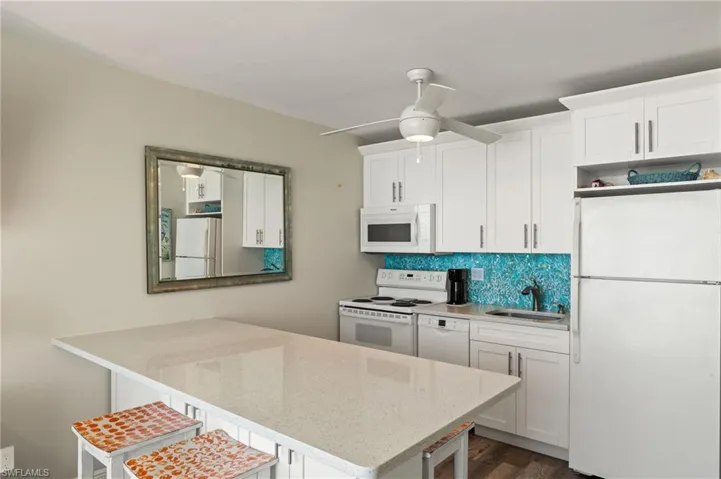 Kitchen with white appliances, sink, light stone counters, a kitchen breakfast bar, and white cabinets