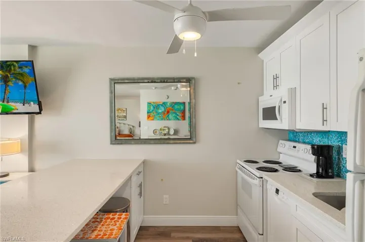Kitchen with white cabinetry, white appliances, hardwood / wood-style floors, and light stone counters