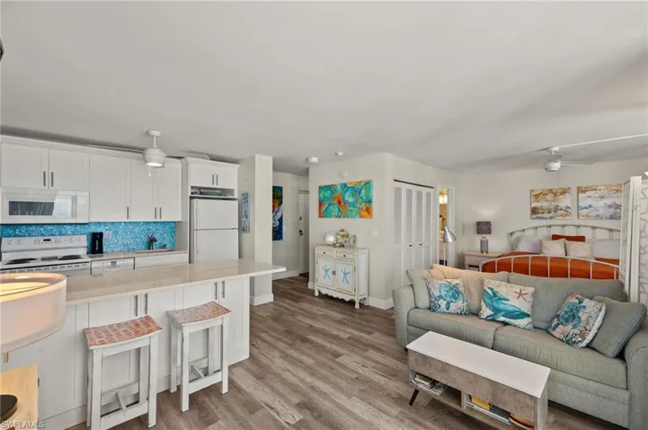 Kitchen featuring white cabinetry, light hardwood / wood-style floors, white appliances, ceiling fan, and a breakfast bar area