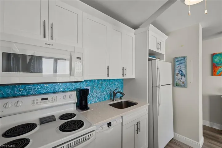 Kitchen featuring white appliances, wood-type flooring, sink, backsplash, and white cabinets