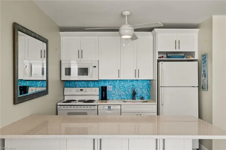Kitchen featuring white appliances, sink, backsplash, light stone counters, and white cabinetry