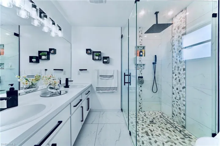 Full bath featuring marble look tiles, a marble finish shower, and double vanity