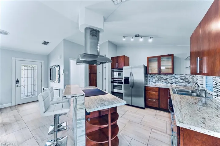 Kitchen featuring lofted ceiling, tasteful backsplash, island range hood, stainless steel refrigerator with ice dispenser, and open shelves