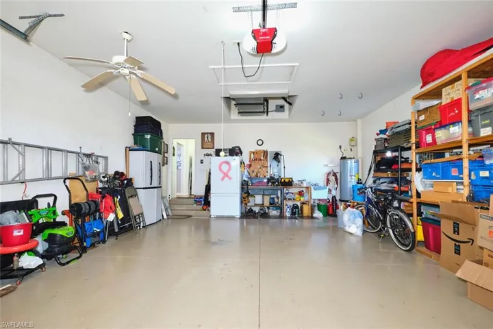 Garage with freestanding refrigerator, electric water heater, a garage door opener, and ceiling fan