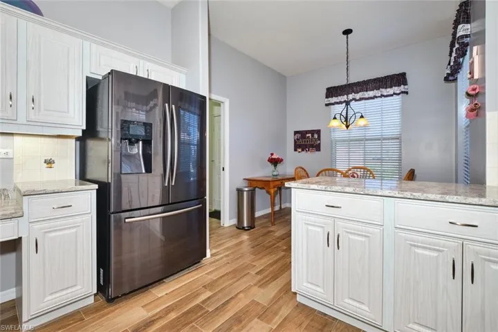 Kitchen with stainless steel refrigerator with ice dispenser, light stone counters, white cabinets, light wood-style floors, and tasteful backsplash