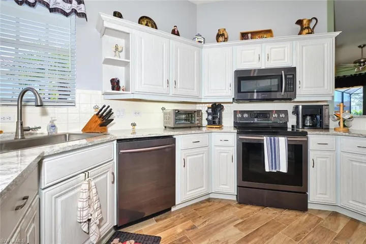 Kitchen featuring stainless steel appliances, white cabinets, light stone countertops, open shelves, and decorative backsplash