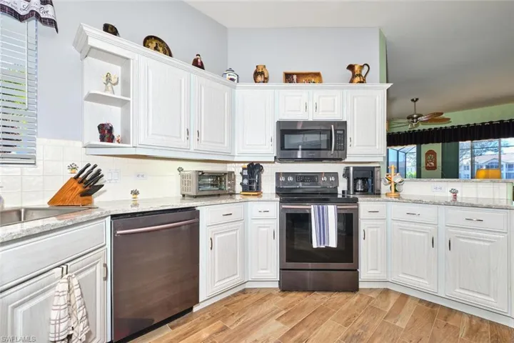 Kitchen featuring stainless steel appliances, white cabinets, open shelves, and decorative backsplash
