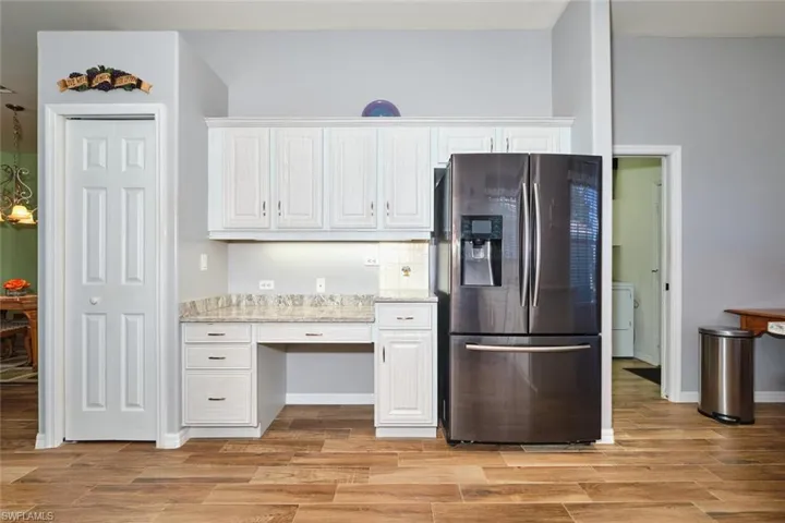 Kitchen featuring stainless steel refrigerator with ice dispenser, wood finish floors, light stone counters, and white cabinets