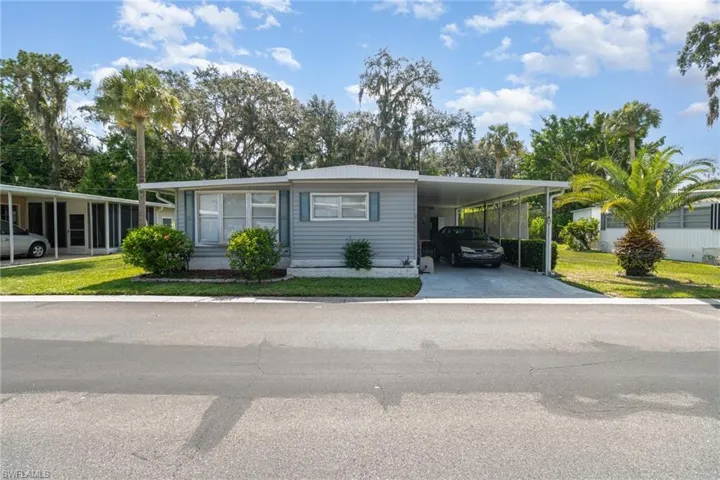 Manufactured / mobile home with an attached carport, a front yard, driveway, and a metal roof