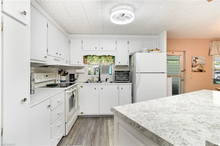 Kitchen with white appliances, white cabinets, light wood-type flooring, light countertops, and under cabinet range hood