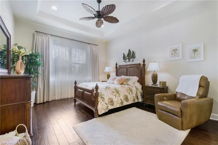 Bedroom featuring ornamental molding, a tray ceiling, dark wood-type flooring, a ceiling fan, and recessed lighting