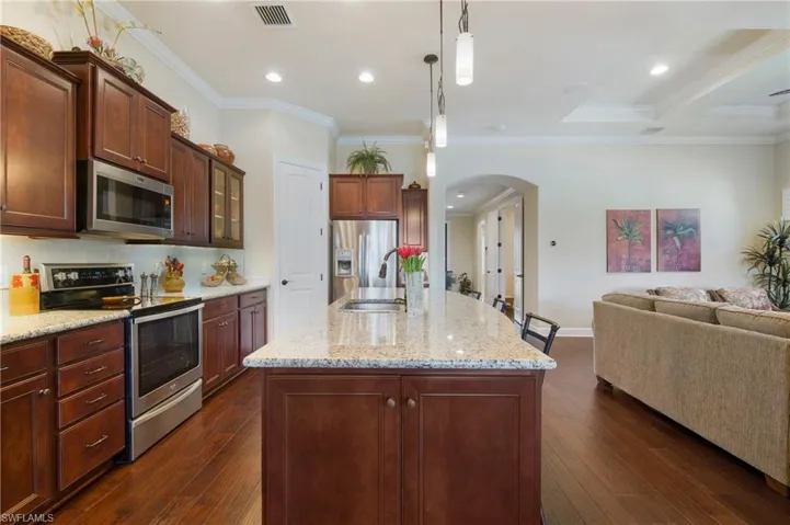 Kitchen featuring appliances with stainless steel finishes, arched walkways, open floor plan, dark wood-type flooring, and light stone counters
