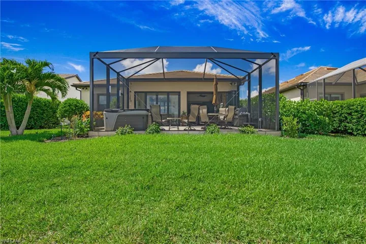 Back of property featuring a hot tub, a patio area, a yard, a lanai, and stucco siding