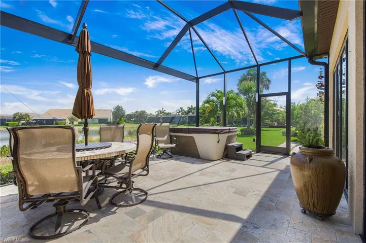 View of patio / terrace featuring a lanai, a hot tub, outdoor dining area, and a water view