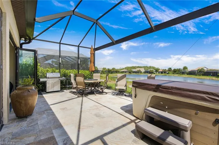 View of patio / terrace with a hot tub, area for grilling, outdoor dining space, glass enclosure, and a water view