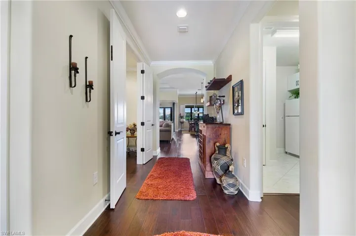Corridor with arched walkways, wood finished floors, and crown molding
