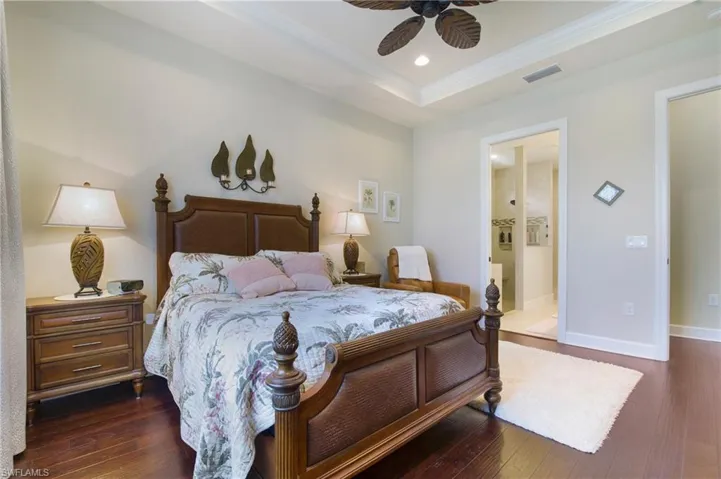 Bedroom with dark wood-style floors, a tray ceiling, crown molding, recessed lighting, and connected bathroom