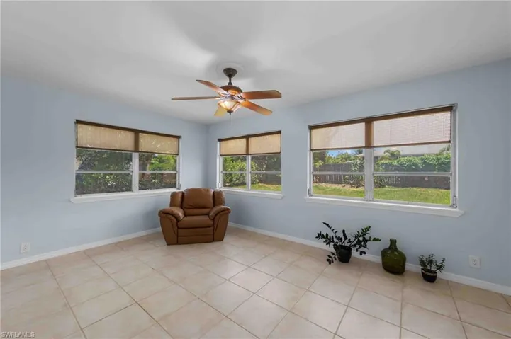 Living area with a ceiling fan, light tile patterned floors, and baseboards