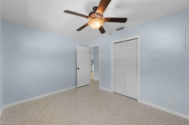 Unfurnished bedroom featuring a closet, speckle patterned floor, baseboards, and a ceiling fan