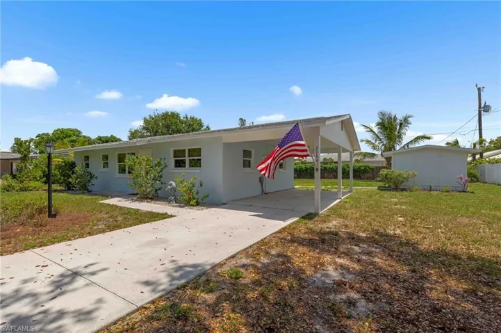 Ranch-style home with driveway, a front yard, an attached carport, and stucco siding