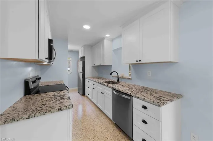 Kitchen featuring appliances with stainless steel finishes, dark aggregate flooring, white cabinetry, light stone countertops, and a sink