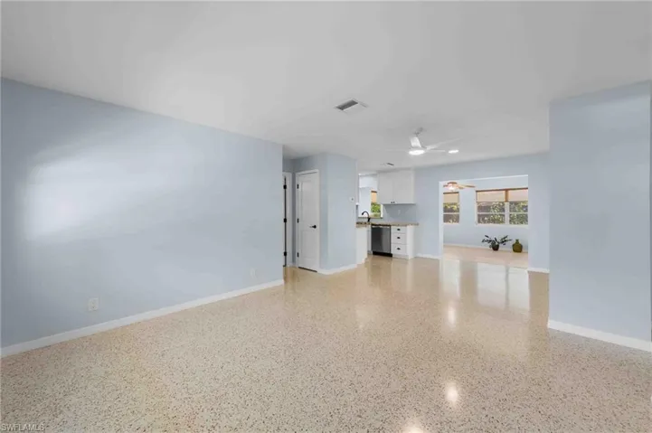 Unfurnished living room with a ceiling fan, dark aggregate flooring, and baseboards