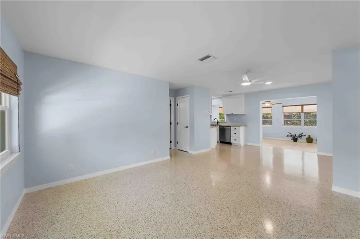 Unfurnished living room featuring a ceiling fan, baseboards, dark speckled floor, and a sink
