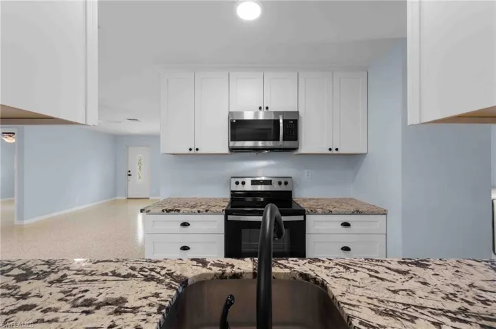 Kitchen featuring stainless steel microwave, electric range oven, baseboards, and light stone countertops