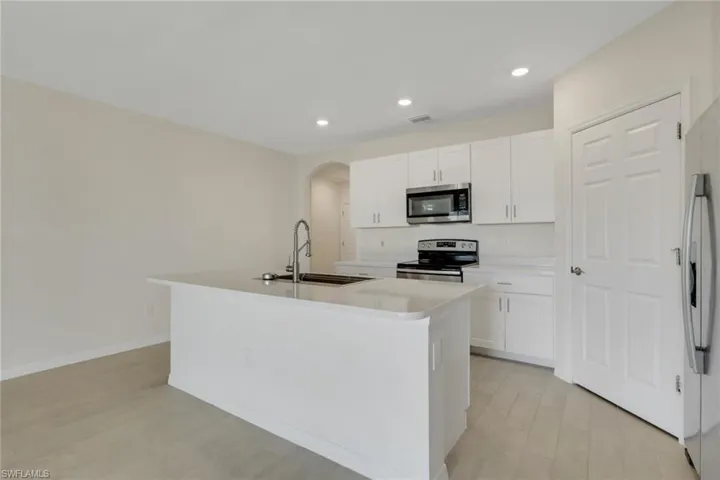 Kitchen featuring arched walkways, white cabinetry, a kitchen island with sink, appliances with stainless steel finishes, and light wood finished floors