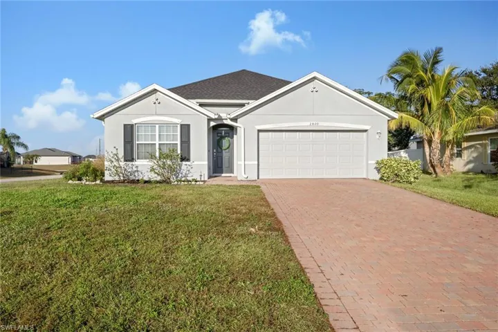 Ranch-style house with stucco siding, a front lawn, decorative driveway, an attached garage, and a shingled roof