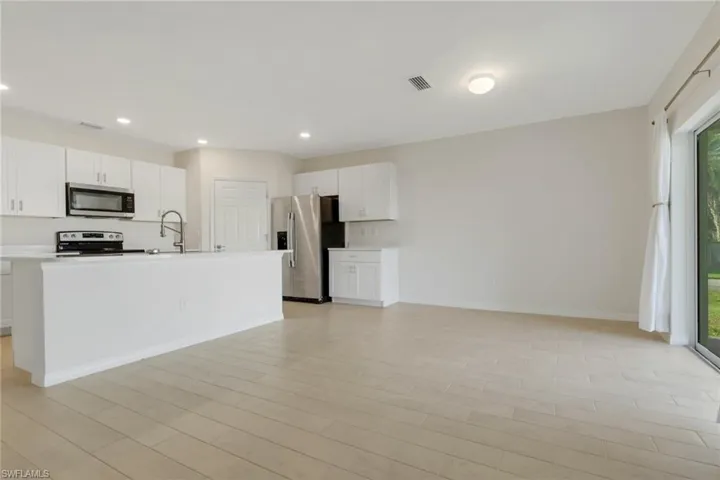 Kitchen with white cabinets, appliances with stainless steel finishes, a kitchen island with sink, light countertops, and recessed lighting