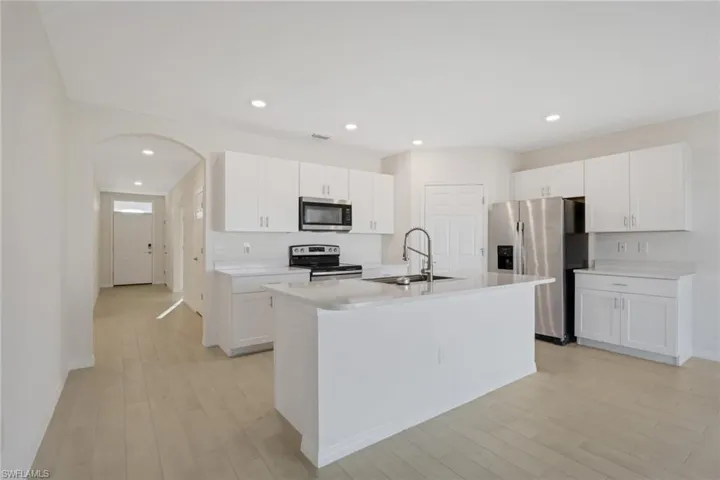 Kitchen with appliances with stainless steel finishes, white cabinets, light wood-type flooring, recessed lighting, and a center island with sink