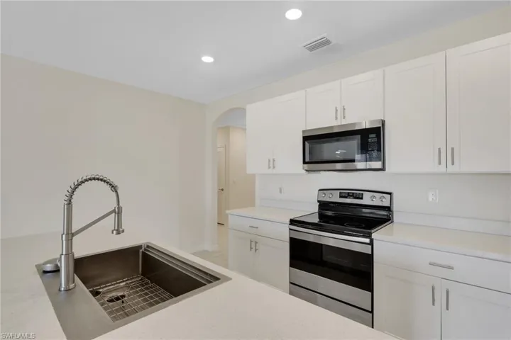 Kitchen featuring stainless steel appliances, white cabinetry, recessed lighting, arched walkways, and light stone counters
