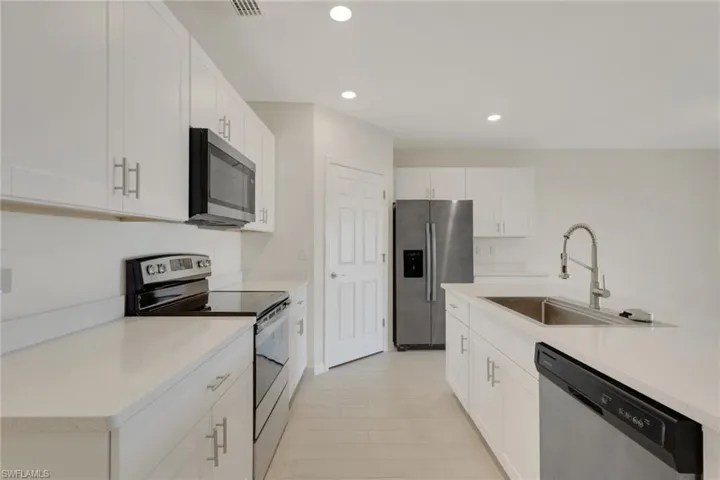 Kitchen featuring appliances with stainless steel finishes, white cabinets, recessed lighting, and light stone countertops