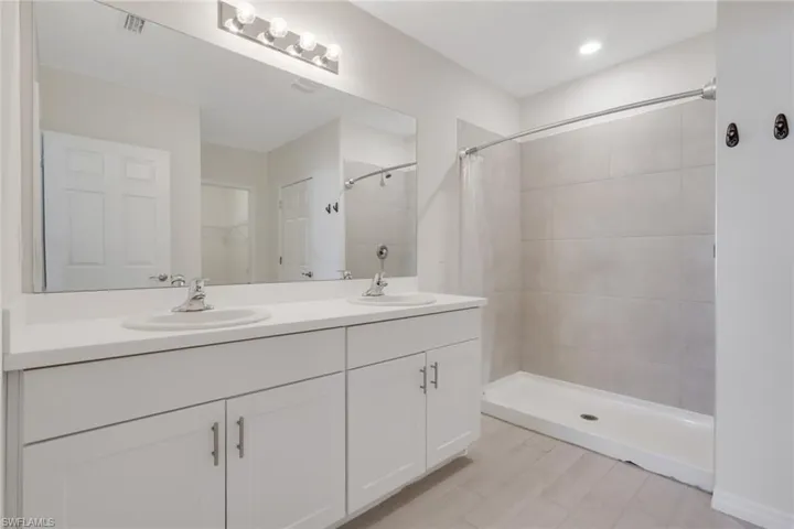 Full bathroom featuring double vanity, a stall shower, and a spacious closet