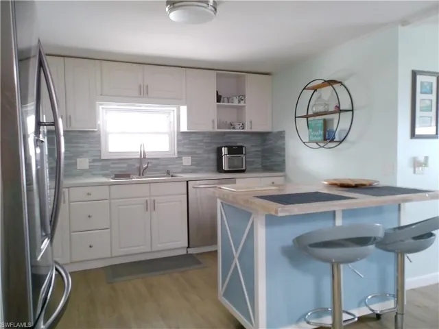 Kitchen with stainless steel appliances, light wood-style floors, white cabinets, a kitchen breakfast bar, and decorative backsplash