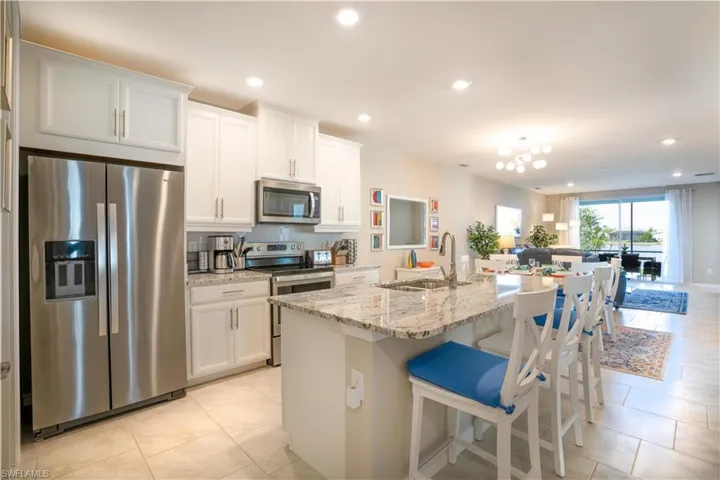 Kitchen with sink, light tile patterned floors, appliances with stainless steel finishes, white cabinetry, and a center island with sink