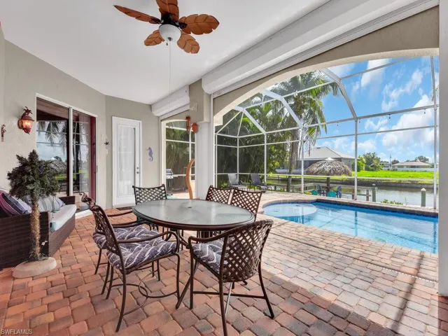 View of swimming pool with glass enclosure, a water view, a patio, and ceiling fan