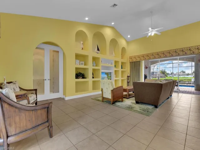 Living room with built in shelves, french doors, light tile patterned flooring, high vaulted ceiling, and ceiling fan