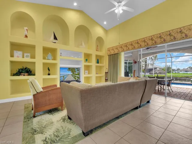 Living room with ceiling fan, tile patterned floors, built in shelves, and high vaulted ceiling