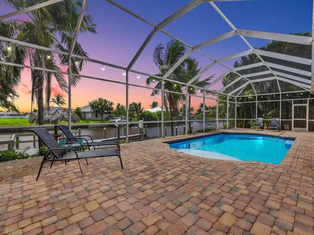 Pool at dusk featuring a patio, a water view, and a lanai
