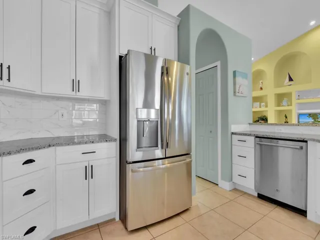 Kitchen with tasteful backsplash, light tile patterned flooring, stainless steel appliances, white cabinetry, and light stone countertops