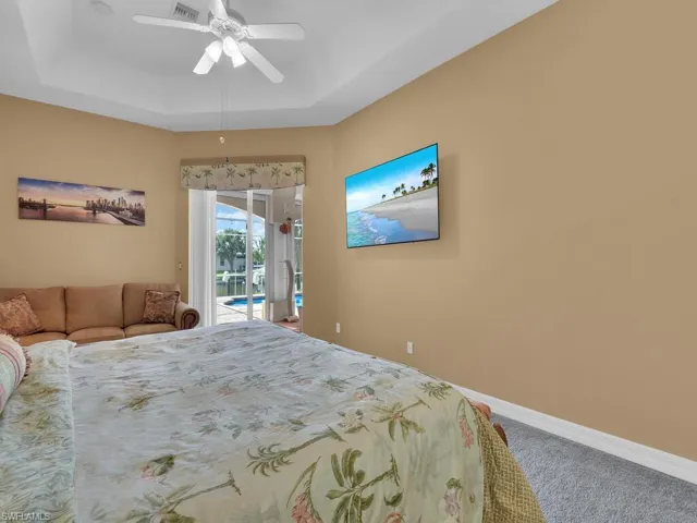 Carpeted bedroom with access to outside, ceiling fan, and a raised ceiling