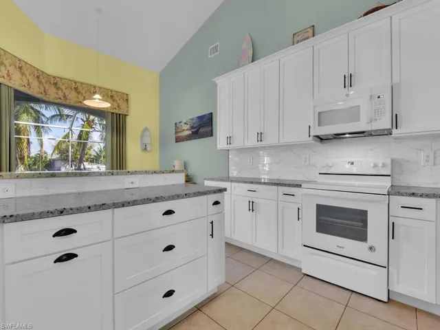Kitchen with lofted ceiling, decorative light fixtures, white cabinets, light tile patterned flooring, and white appliances