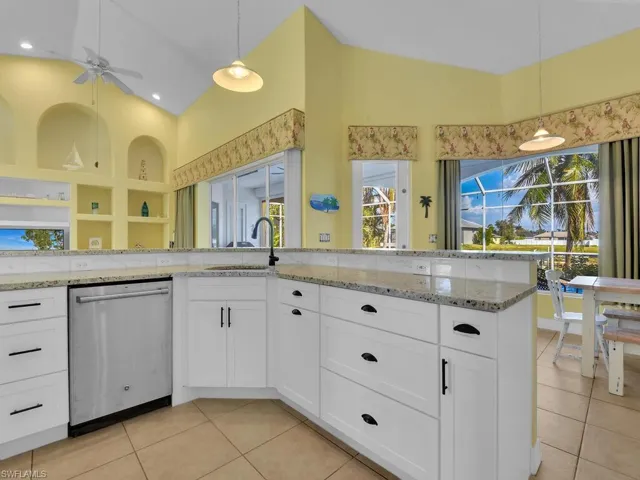 Kitchen with white cabinetry, decorative light fixtures, light stone countertops, sink, and stainless steel dishwasher