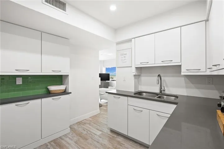 Kitchen with sink, white cabinetry, light hardwood / wood-style flooring, and tasteful backsplash