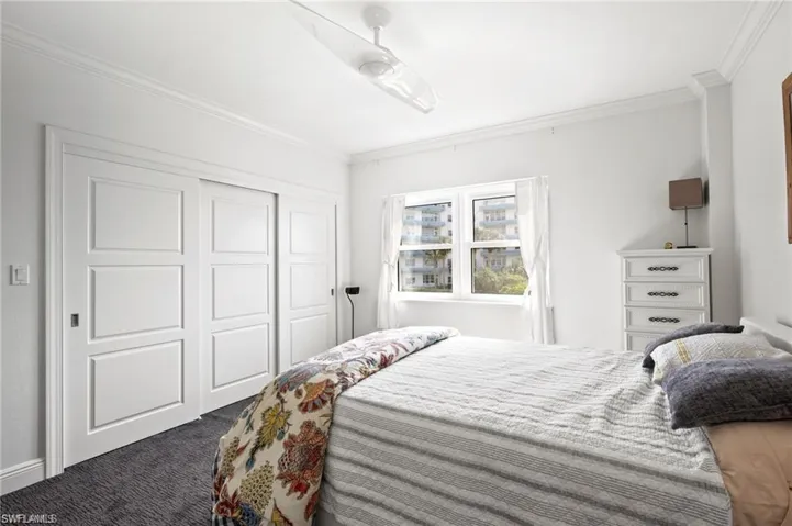 Bedroom featuring ceiling fan, a closet, crown molding, and dark carpet