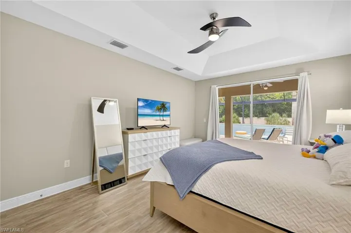 Bedroom with a tray ceiling, light wood finished floors, access to outside, and ceiling fan