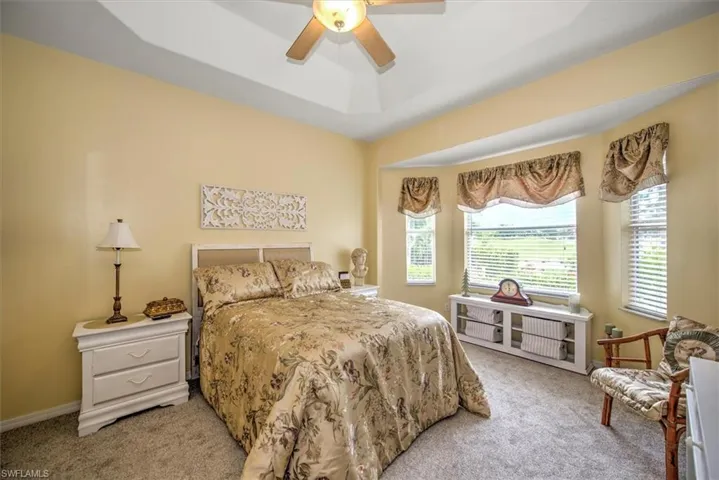 Carpeted bedroom featuring ceiling fan and a raised ceiling