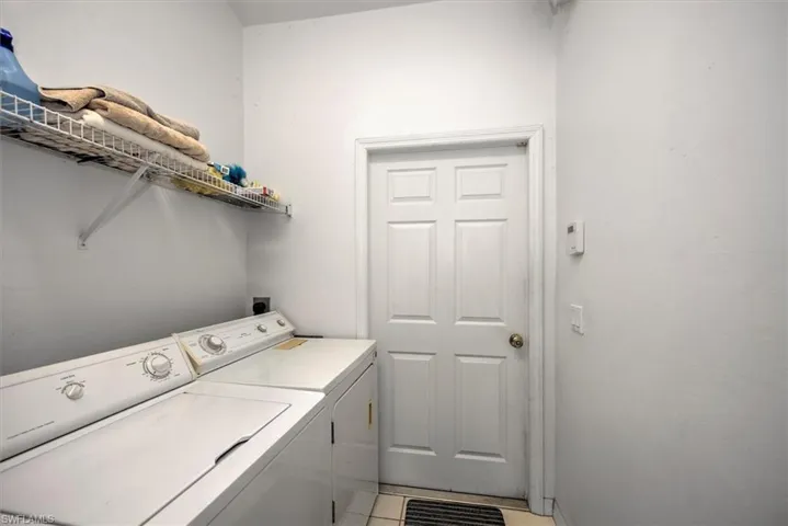 Washroom with light tile flooring and washing machine and dryer